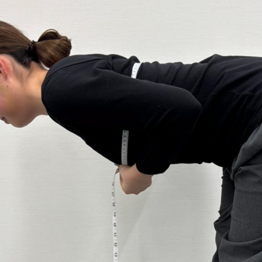 お辞儀姿勢でトップバストを測っている女性のイメージ写真